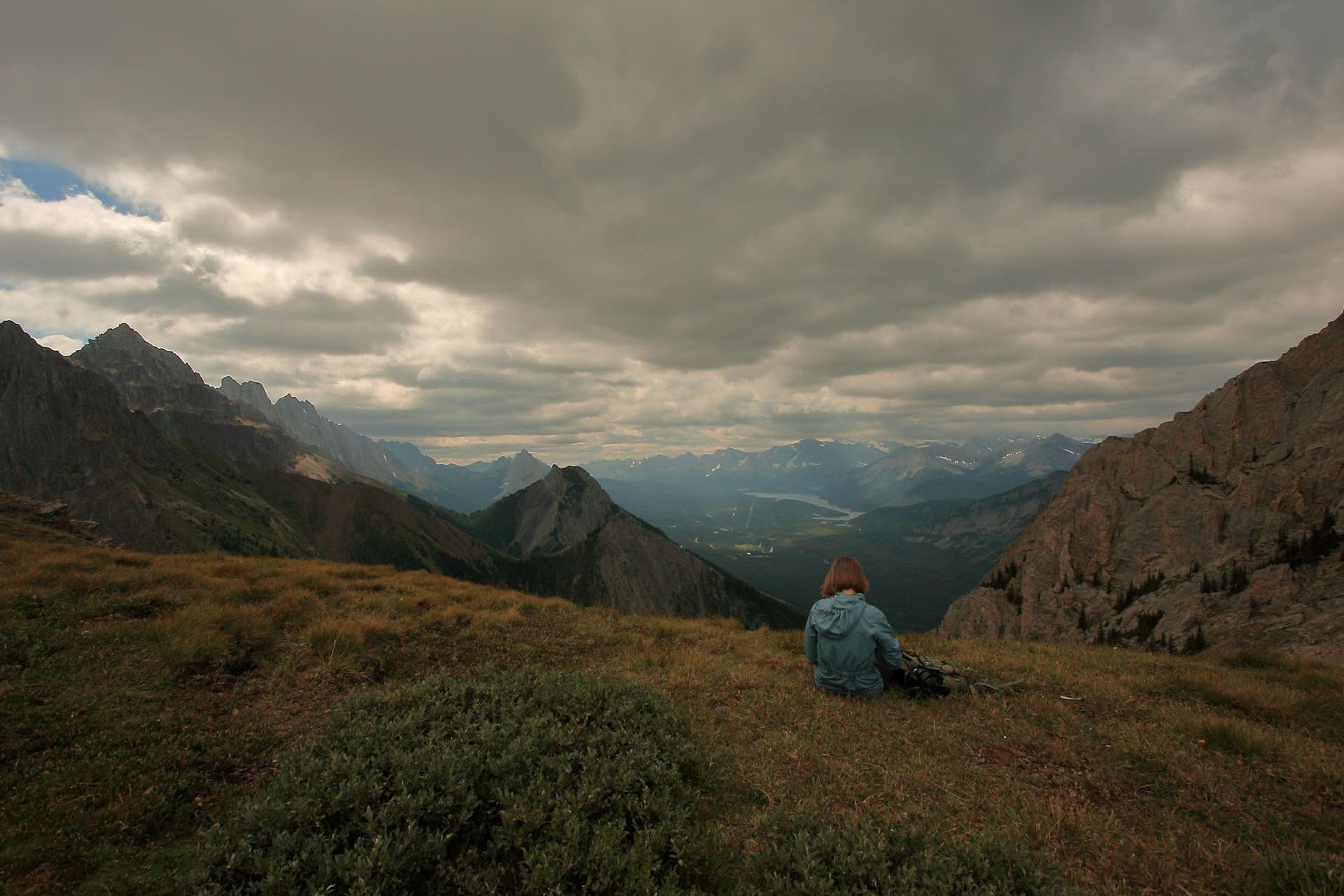 A lone walker sitting above a wide mountain valley